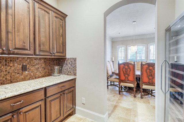 kitchen featuring light stone counters, decorative backsplash, ornamental molding, and decorative light fixtures