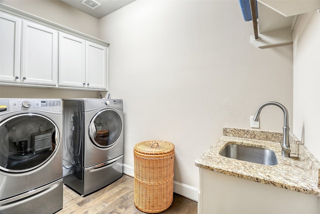 washroom featuring cabinets, sink, washing machine and clothes dryer, and light wood-type flooring