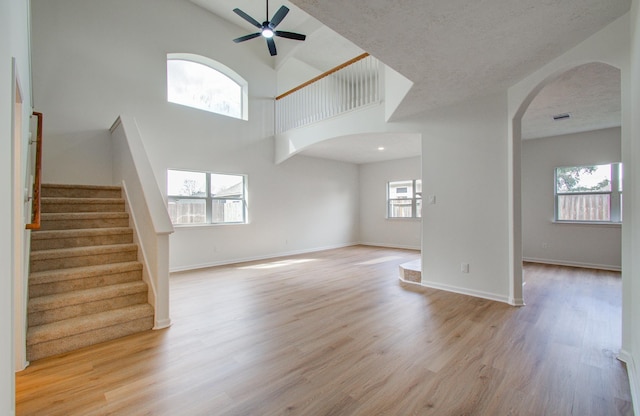 unfurnished living room featuring ceiling fan, a textured ceiling, light hardwood / wood-style flooring, and a high ceiling