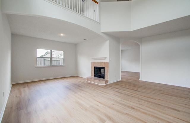 unfurnished living room featuring a tile fireplace, light hardwood / wood-style flooring, and a high ceiling