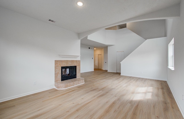 unfurnished living room with a tiled fireplace, high vaulted ceiling, and light wood-type flooring