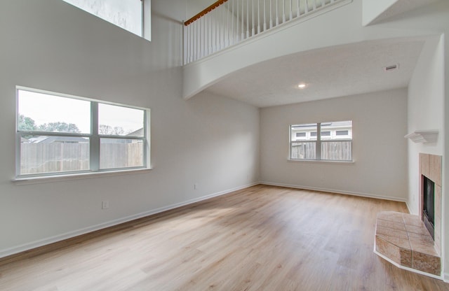 unfurnished living room with a tiled fireplace, plenty of natural light, a high ceiling, and light hardwood / wood-style floors