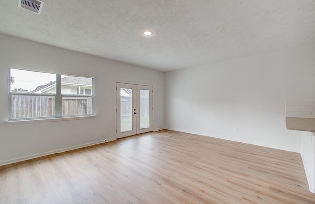 empty room with french doors, a textured ceiling, and light wood-type flooring