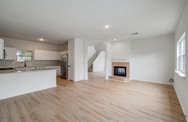 kitchen with white cabinetry, decorative backsplash, a tiled fireplace, stainless steel fridge with ice dispenser, and light wood-type flooring