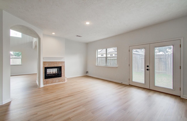 unfurnished living room featuring a fireplace, light hardwood / wood-style floors, french doors, and a textured ceiling