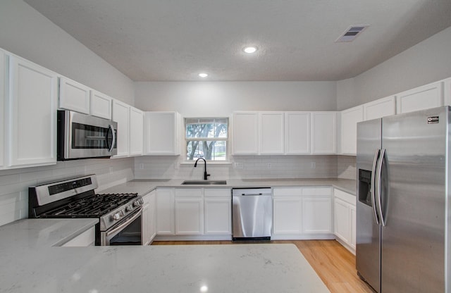 kitchen with sink, white cabinetry, light stone counters, appliances with stainless steel finishes, and light hardwood / wood-style floors