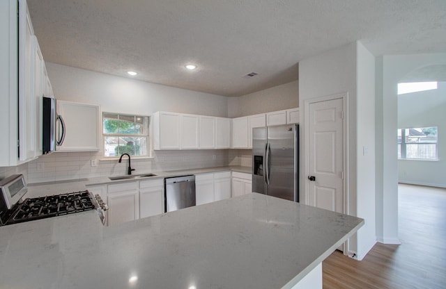 kitchen featuring sink, stainless steel appliances, light stone counters, decorative backsplash, and kitchen peninsula