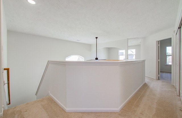 hall with light colored carpet and a textured ceiling