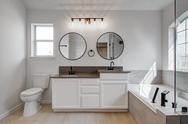 bathroom with vanity, tiled bath, and toilet