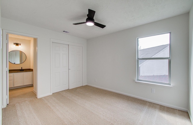 unfurnished bedroom with ensuite bath, light colored carpet, a textured ceiling, a closet, and ceiling fan