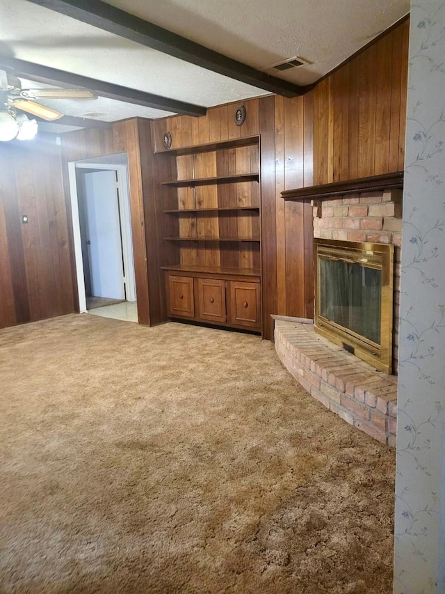 unfurnished living room featuring beam ceiling, light carpet, a textured ceiling, wooden walls, and a fireplace