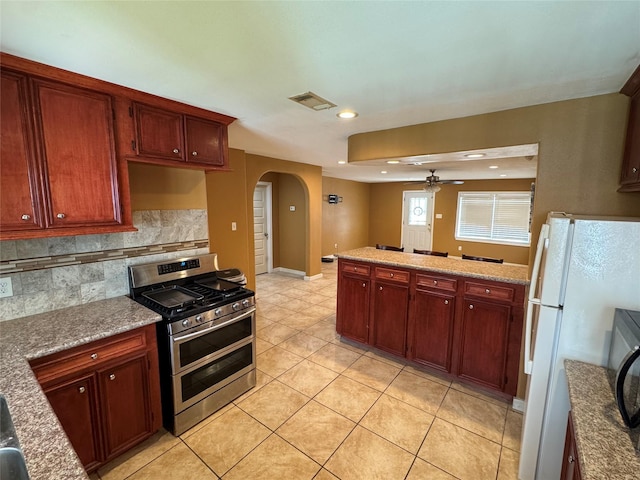 kitchen featuring light tile patterned floors, ceiling fan, white refrigerator, decorative backsplash, and range with two ovens