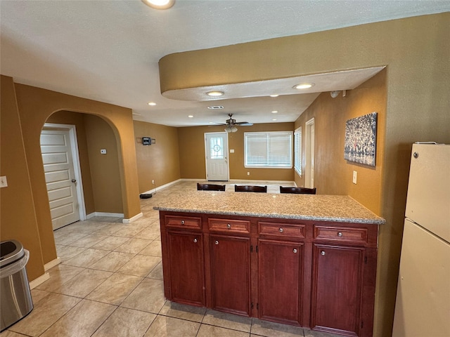 kitchen with light stone countertops, white fridge, light tile patterned flooring, and ceiling fan