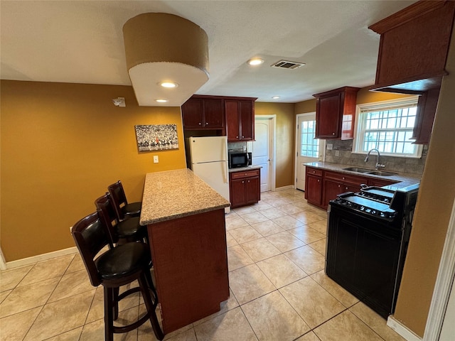 kitchen with sink, backsplash, a kitchen breakfast bar, black range, and white fridge