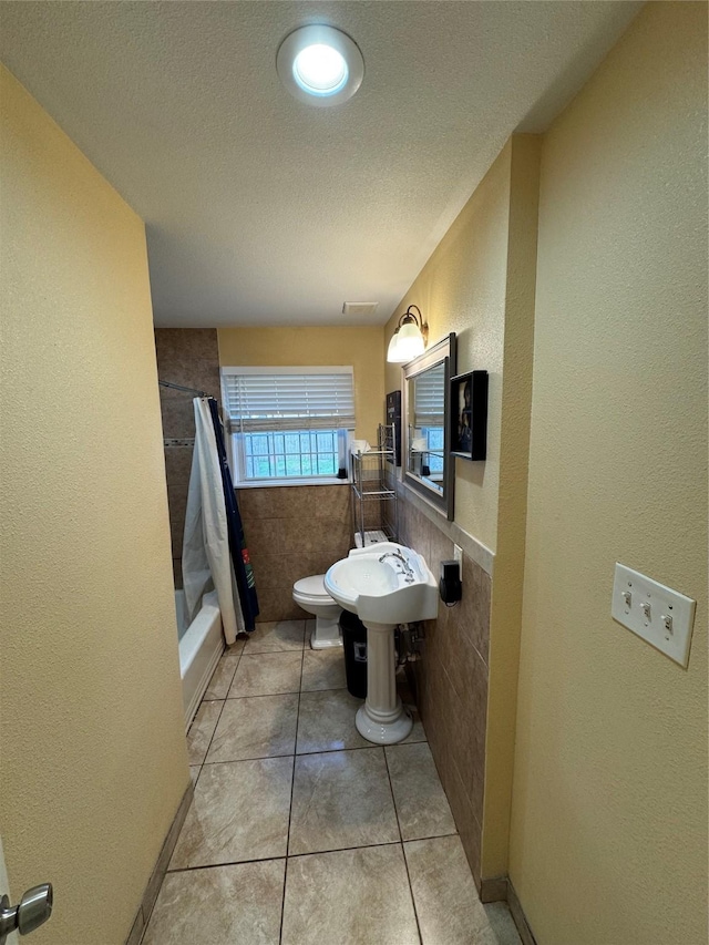 bathroom with tile patterned floors, toilet, tile walls, a textured ceiling, and shower / bathtub combination with curtain