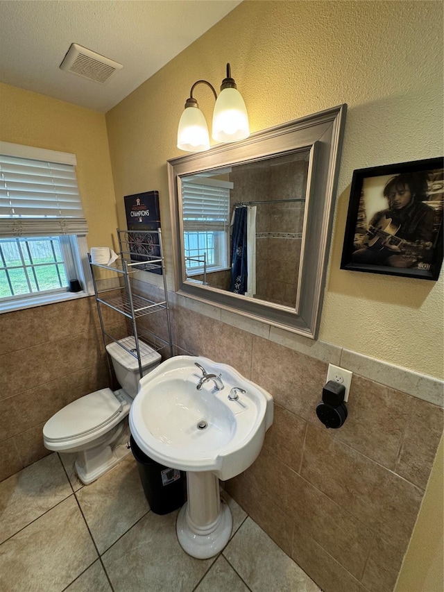 bathroom with tile patterned floors, toilet, sink, and tile walls