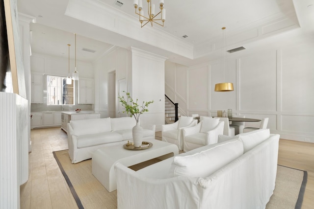 living room with a tray ceiling, ornamental molding, light hardwood / wood-style floors, and a chandelier