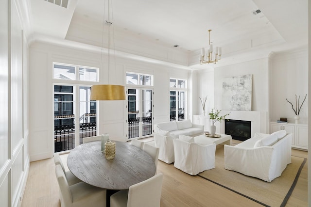 living room with an inviting chandelier, a raised ceiling, a high ceiling, and light wood-type flooring