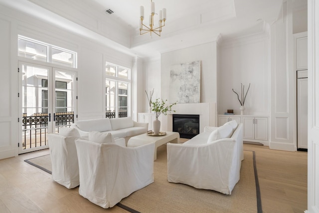 living room with ornamental molding, a tray ceiling, a chandelier, and light hardwood / wood-style floors