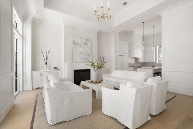 living room with a raised ceiling, crown molding, a chandelier, and light hardwood / wood-style flooring