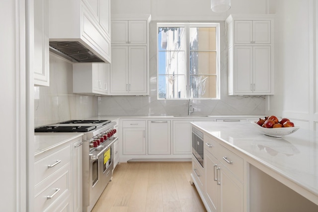 kitchen with white cabinetry, sink, light stone counters, stainless steel appliances, and custom range hood