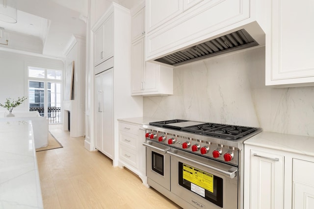 kitchen featuring light stone counters, double oven range, wall chimney range hood, and white cabinets