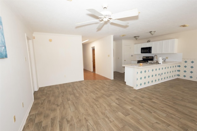 unfurnished living room with ceiling fan, light wood-style floors, visible vents, and a sink