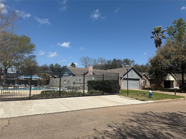 exterior space featuring concrete driveway, a swimming pool, an attached garage, and fence