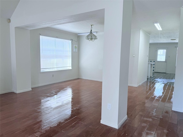 unfurnished room with dark wood finished floors, an inviting chandelier, and baseboards