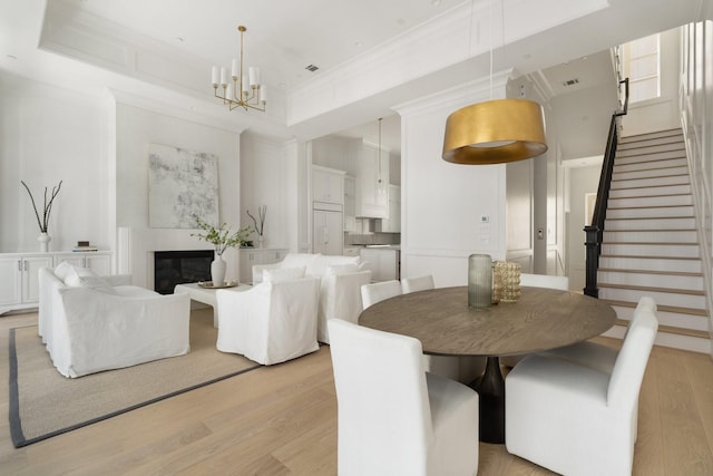 dining area featuring crown molding, a towering ceiling, a notable chandelier, and light hardwood / wood-style floors