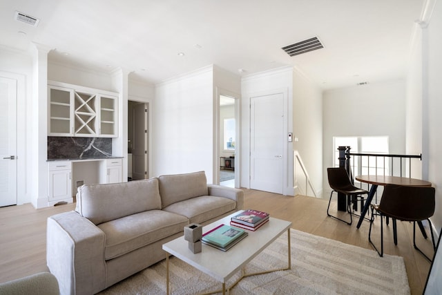 living room featuring crown molding, bar area, light hardwood / wood-style floors, and decorative columns