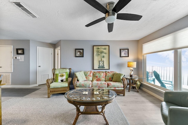 living room featuring ceiling fan, light hardwood / wood-style flooring, and a textured ceiling