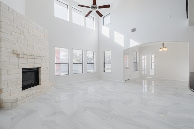 unfurnished living room featuring a stone fireplace, ceiling fan, and french doors