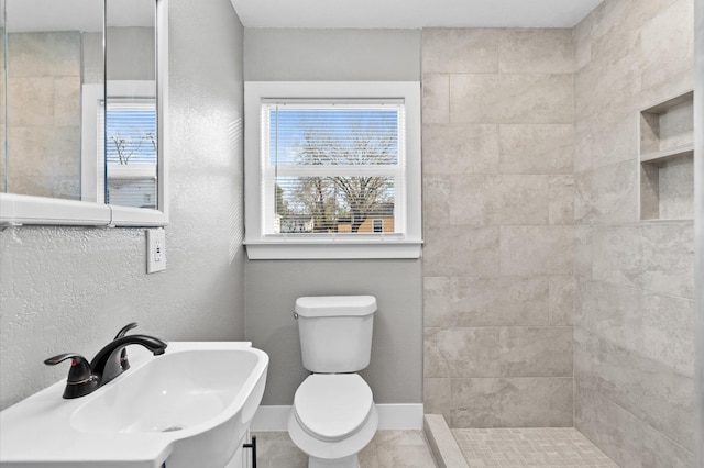 bathroom featuring sink, tiled shower, and toilet