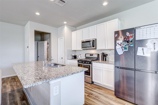 kitchen featuring sink, white cabinetry, stainless steel appliances, light hardwood / wood-style floors, and a center island with sink