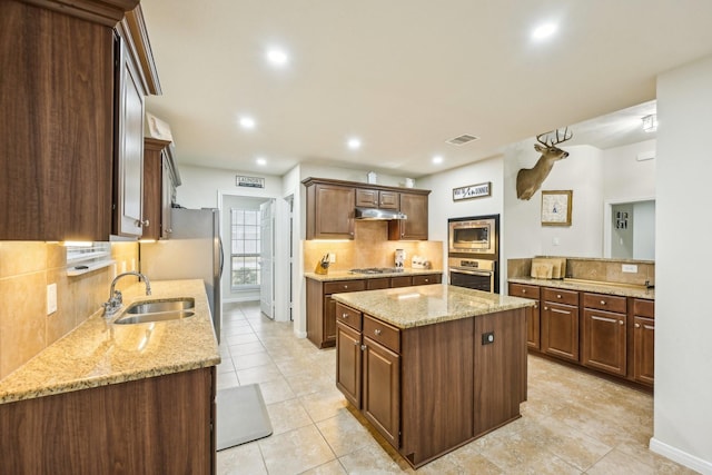 kitchen with sink, backsplash, stainless steel appliances, light stone counters, and a kitchen island