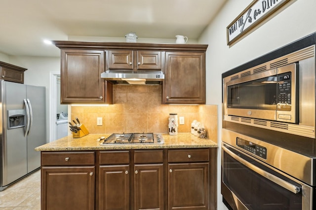 kitchen with tasteful backsplash, light stone countertops, dark brown cabinets, and stainless steel appliances