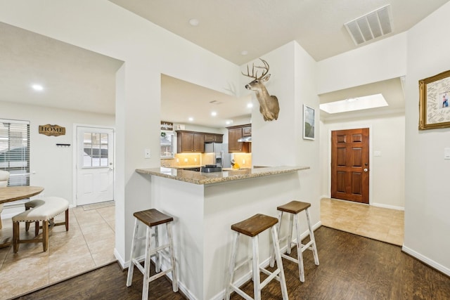 kitchen featuring hardwood / wood-style flooring, stainless steel fridge, a kitchen breakfast bar, light stone countertops, and kitchen peninsula