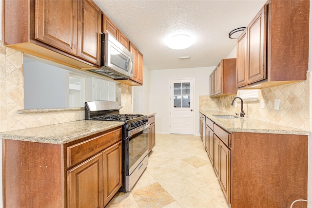 kitchen with sink, light stone counters, a textured ceiling, appliances with stainless steel finishes, and decorative backsplash