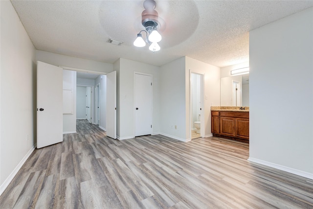 unfurnished bedroom featuring sink, ensuite bath, light hardwood / wood-style flooring, ceiling fan, and a textured ceiling