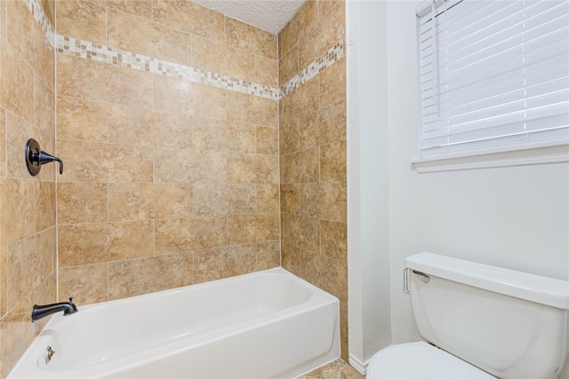 bathroom featuring tiled shower / bath, a textured ceiling, and toilet