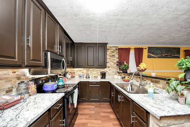 kitchen featuring light wood finished floors, black range with electric stovetop, backsplash, a sink, and dark brown cabinets