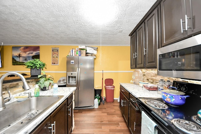 kitchen with a textured ceiling, light wood-style flooring, a sink, dark brown cabinets, and appliances with stainless steel finishes