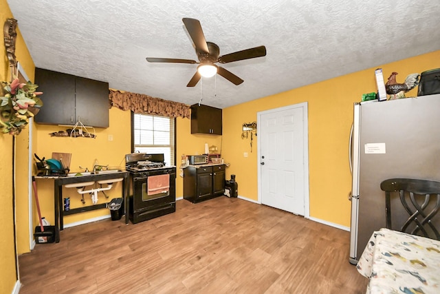 kitchen with light wood finished floors, a ceiling fan, freestanding refrigerator, black range with gas cooktop, and a textured ceiling