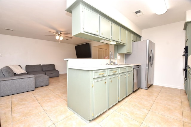 kitchen featuring appliances with stainless steel finishes, green cabinetry, sink, light tile patterned floors, and kitchen peninsula