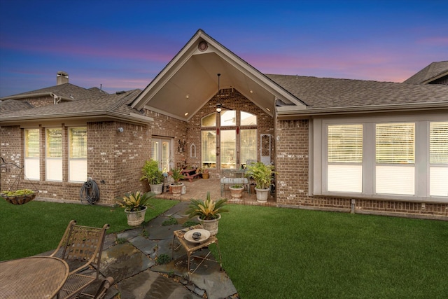 back house at dusk with a patio and a yard