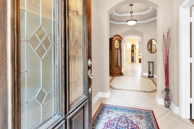 entryway with light tile patterned flooring, crown molding, and a tray ceiling