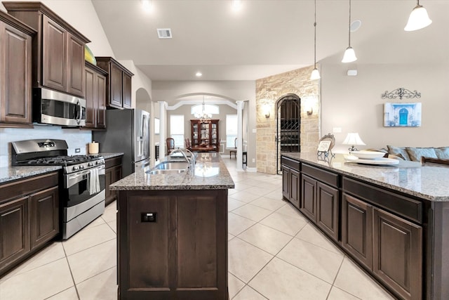 kitchen featuring dark brown cabinetry, sink, hanging light fixtures, a center island with sink, and appliances with stainless steel finishes