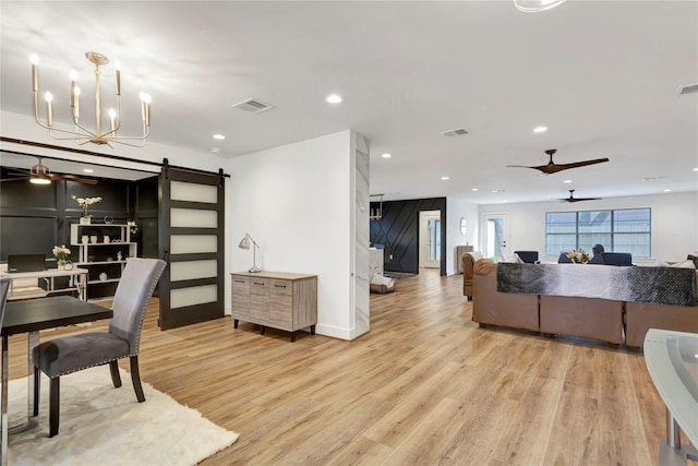 interior space featuring ceiling fan with notable chandelier, light hardwood / wood-style flooring, and a barn door