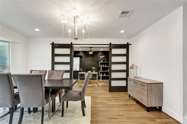 dining room with an inviting chandelier, a barn door, and light wood-type flooring